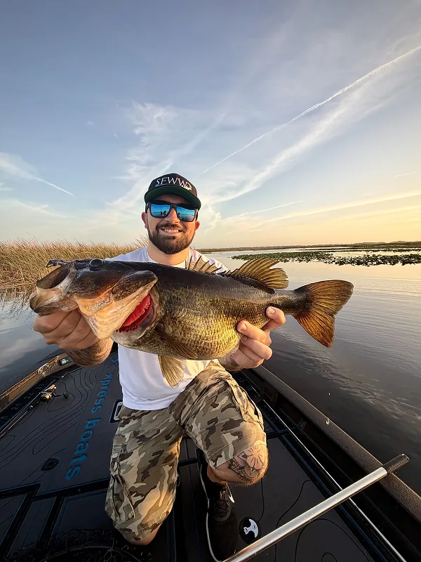 Man kneeling on a boat holding a large bass